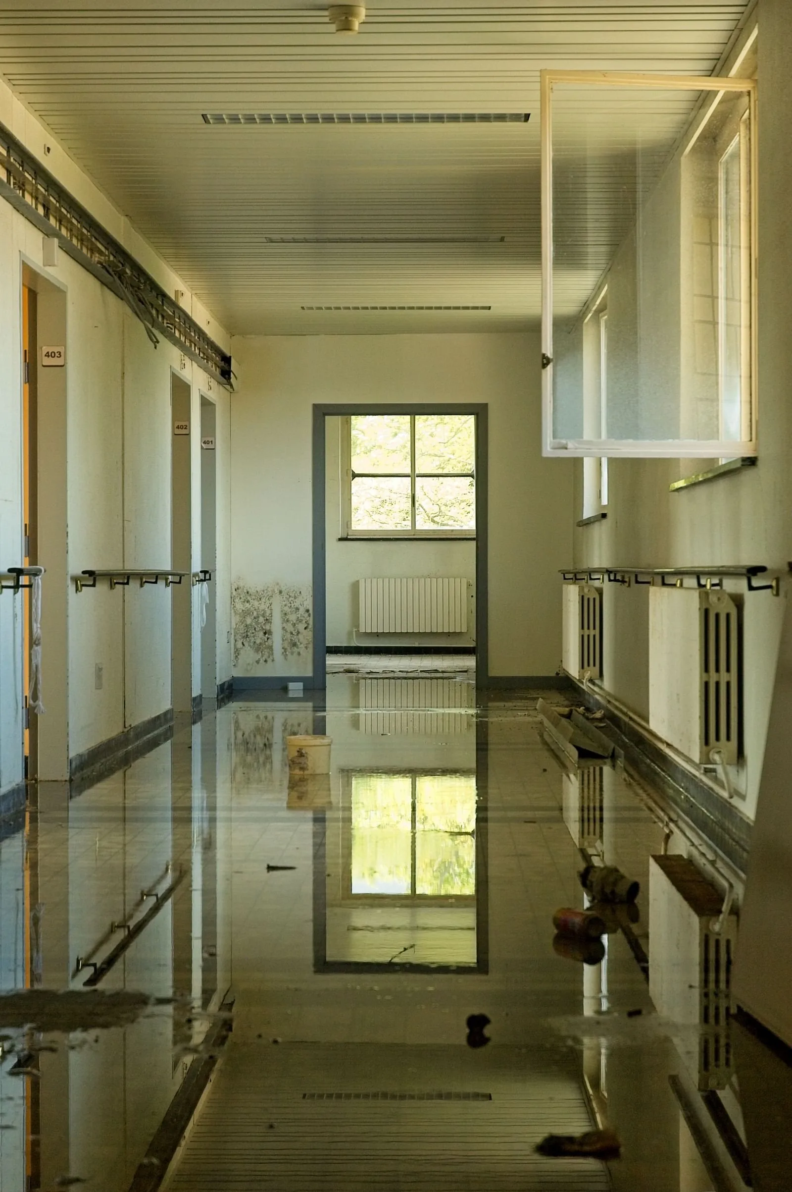 Standing water covering the corridor floor of a damaged institutional building
